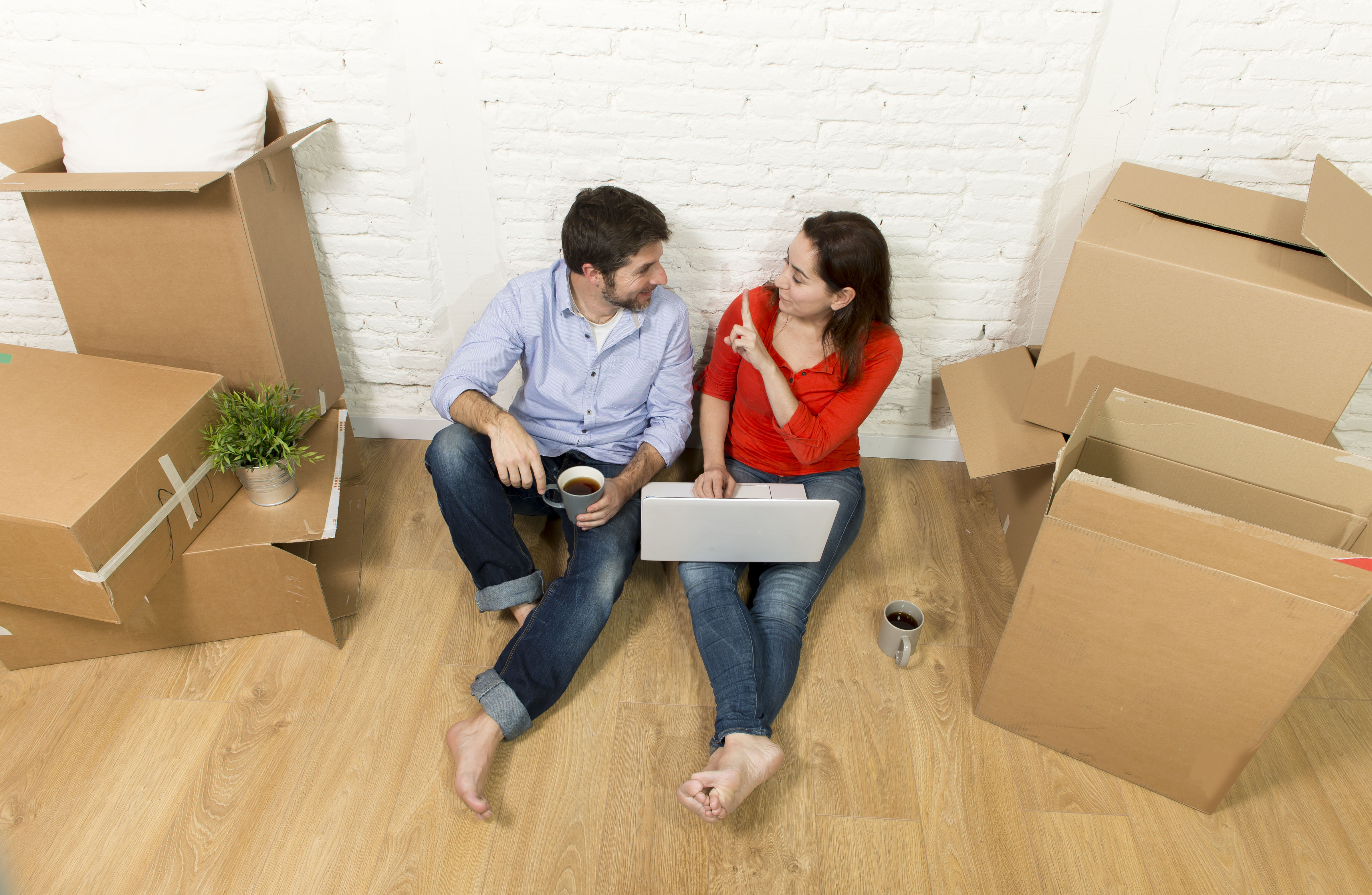 young happy American couple sitting on floor moving in a new house or apartment flat using computer laptop choosing online furniture and household in real estate and independent lifestyle concept